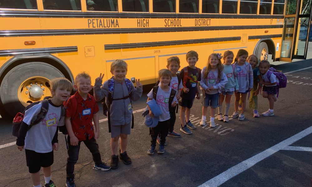 A group of students standing in a line in front of a yellow school bus, smiling for the camera.