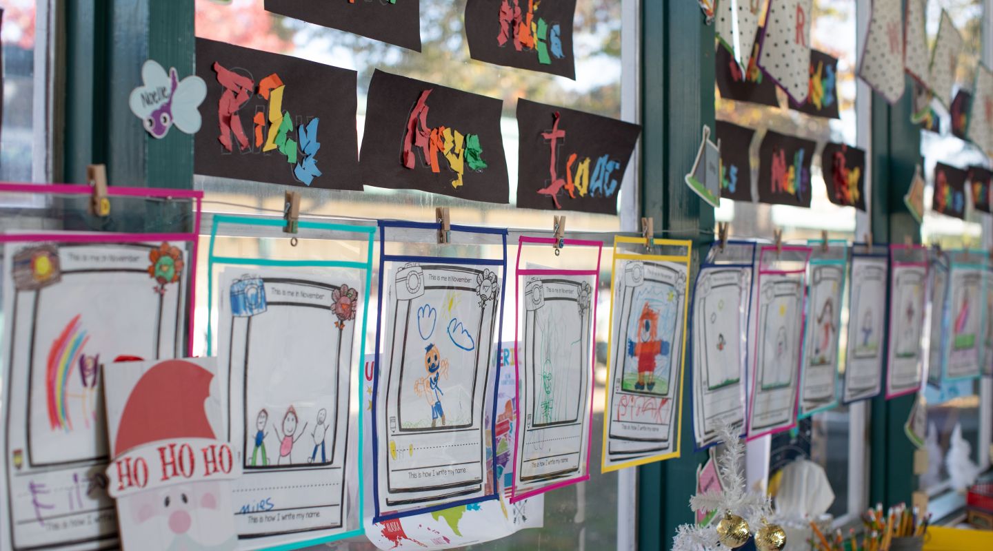 children's school work and art projects hung up on a classroom window.