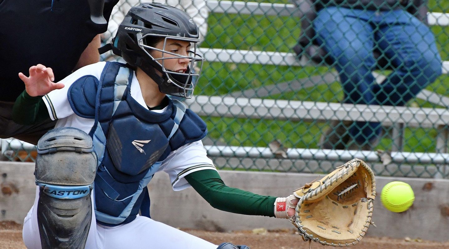 A Casa Grande student playing catcher in a softball game, catching a softball in their mitt.