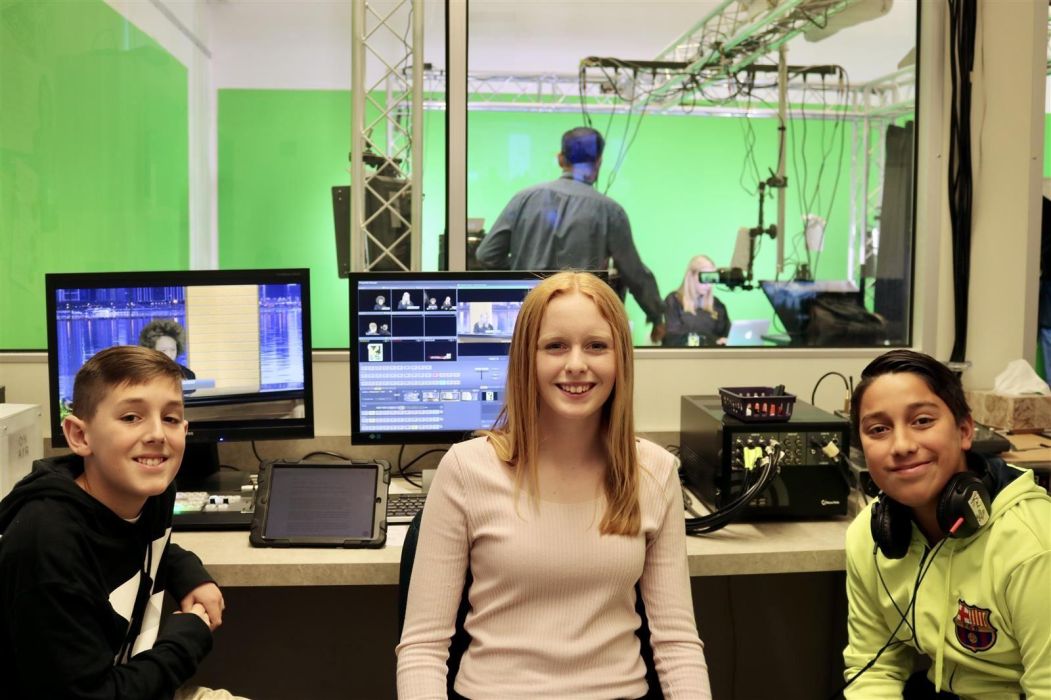 A photo of students smiling at the camera with a view of a green screen film set behind them.